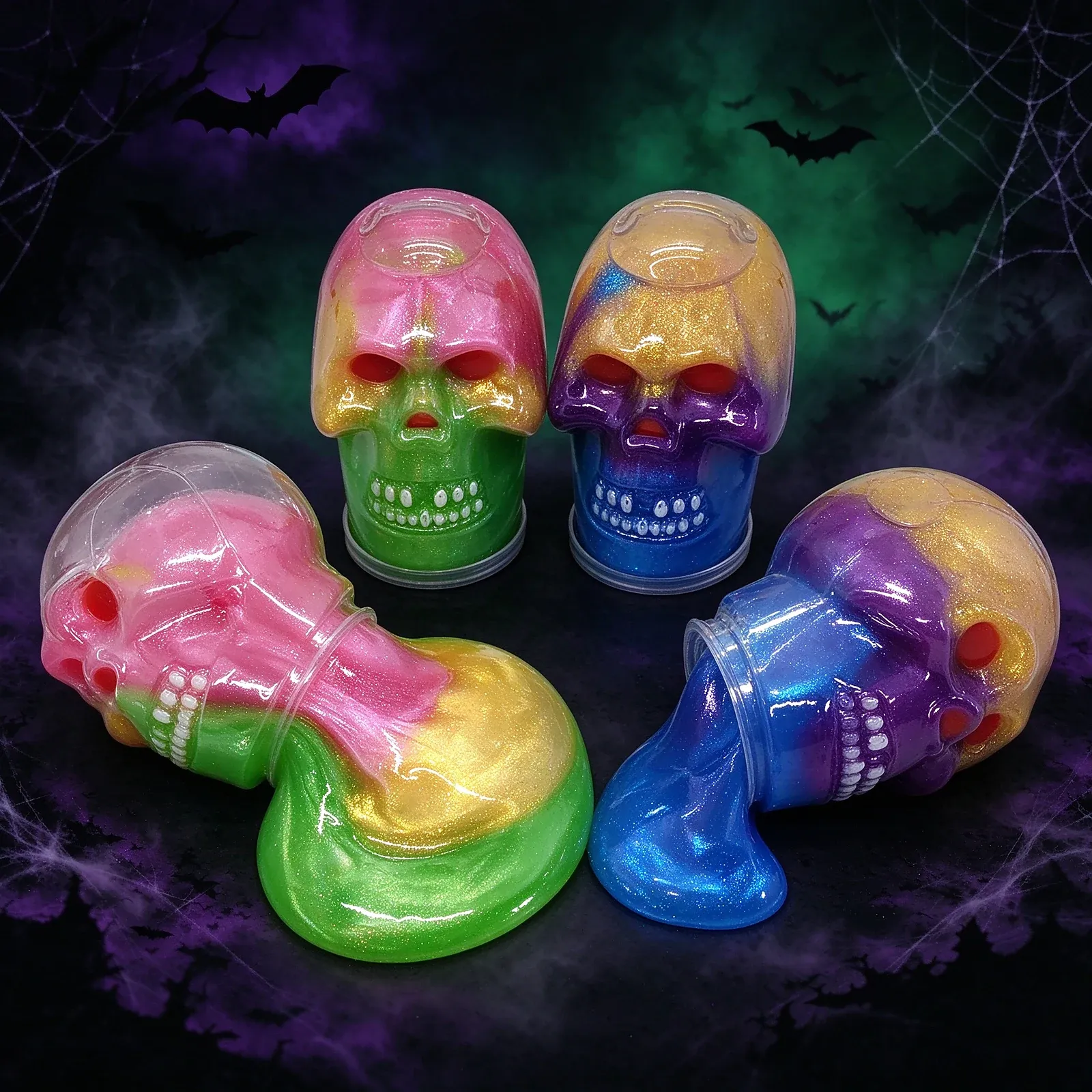 Glitter Skull Slime - Four large translucent skull containers with clear domes, filled with marbled glitter slime in pink-gold-green and blue-purple-gold, with red eyes and a row of white teeth.