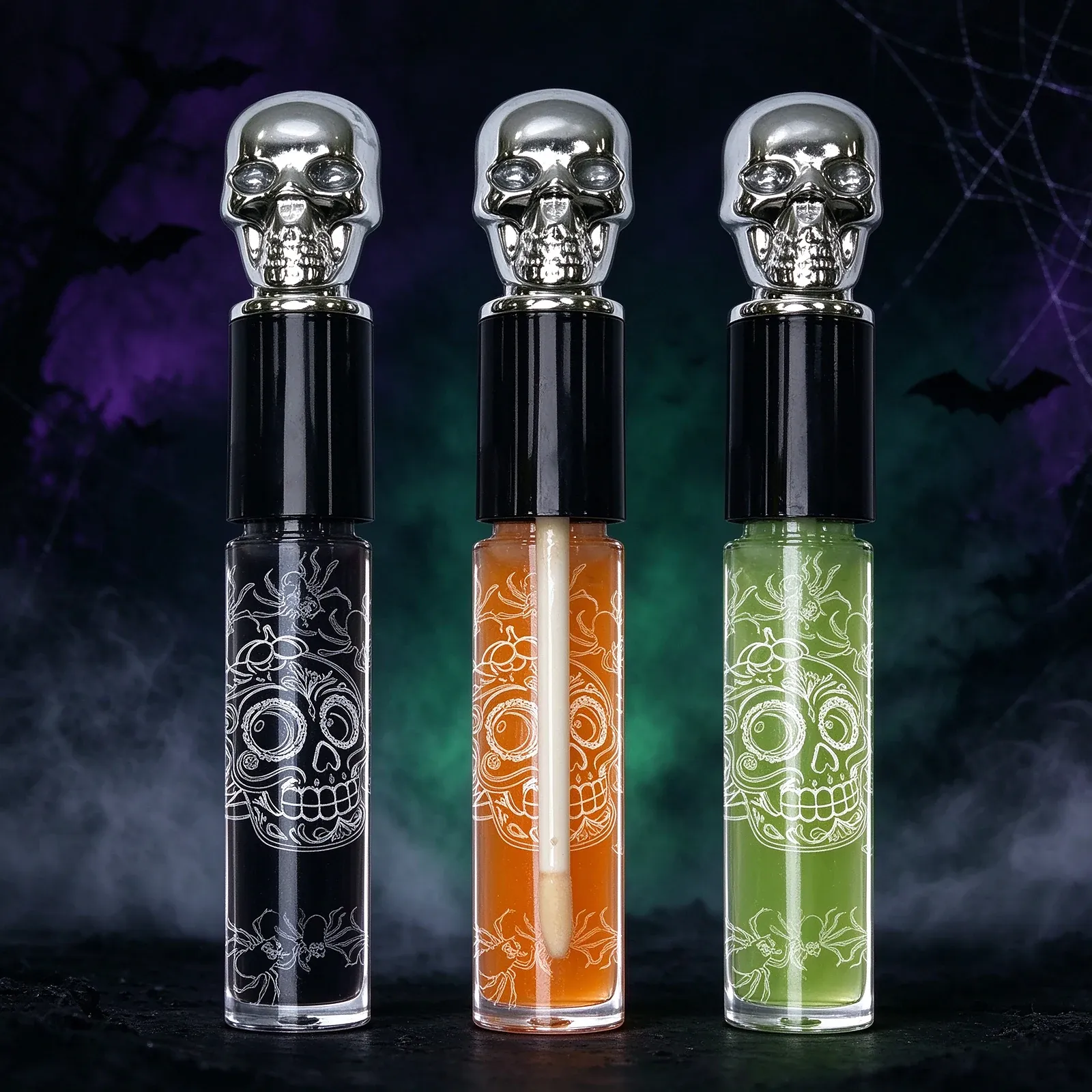 Skull Cap Lip Gloss Set - Three clear gloss tubes topped with chrome skull caps, filled with black, orange and green gloss and printed with a white sugar-skull design, supplied on a black-and-green blister card.