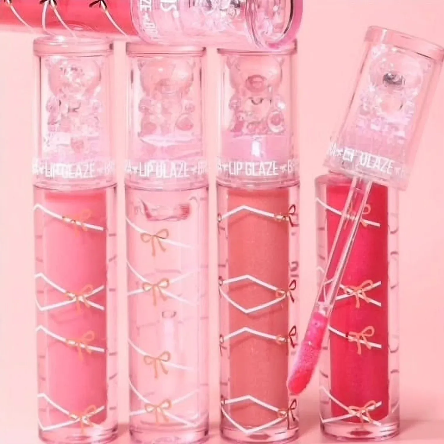 Three pink lip glaze tubes with bow caps arranged in a pink gift box