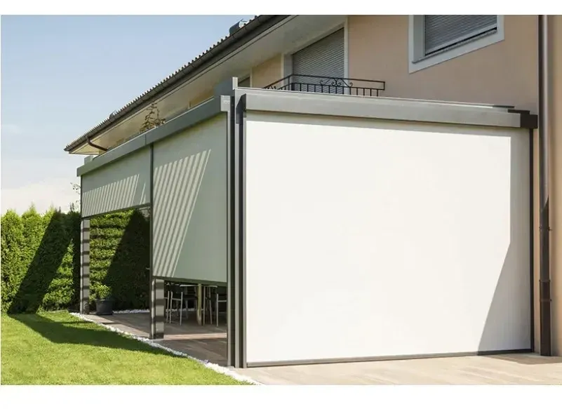 Cordless Spring System manual windproof roller blind installed on an outdoor house terrace, blind lowered, lawn and hedge in the foreground.