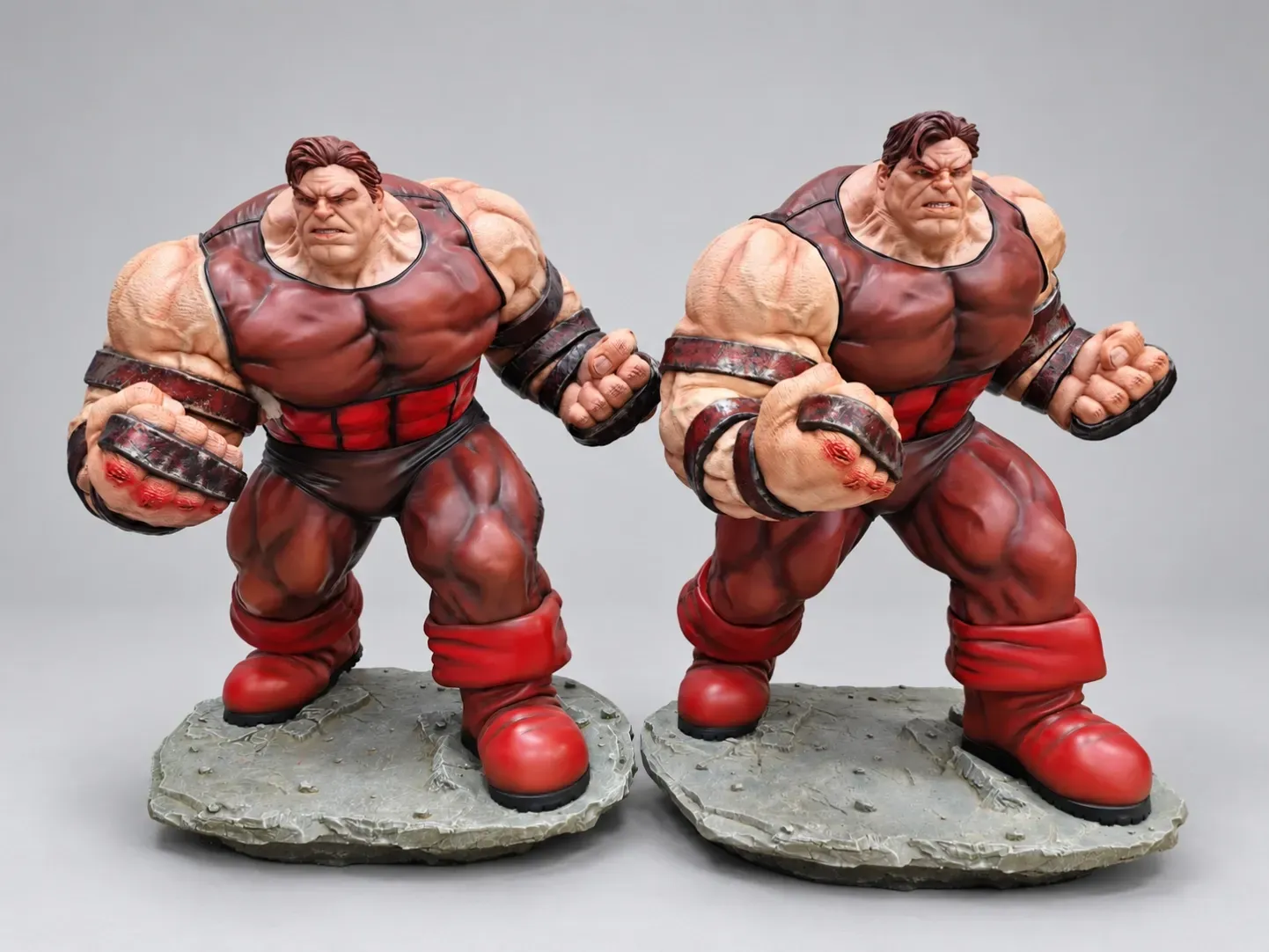Two painted muscular collectible statues side by side on textured bases against a gray background.