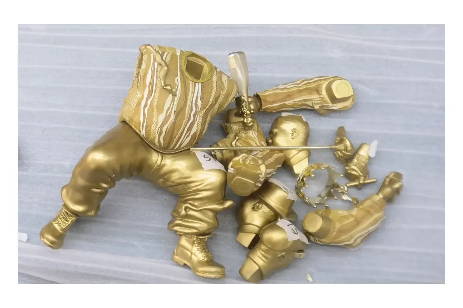 Gold-colored collectible torso, head, limbs and accessories grouped on a pale protective foam sheet before assembly