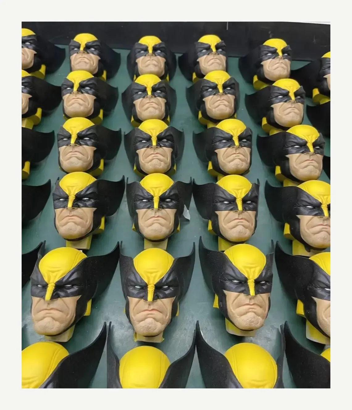 Rows of painted collectible heads with yellow-and-black masks and textured skin on a green work surface