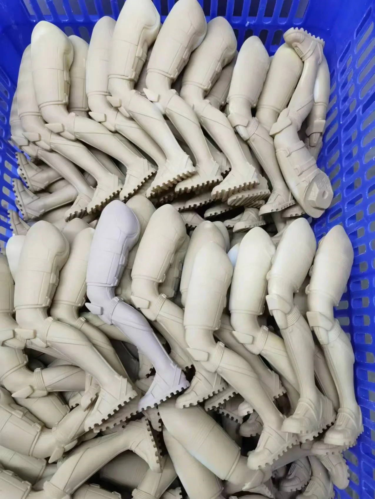 Unpainted collectible leg components arranged in a blue production basket before finishing