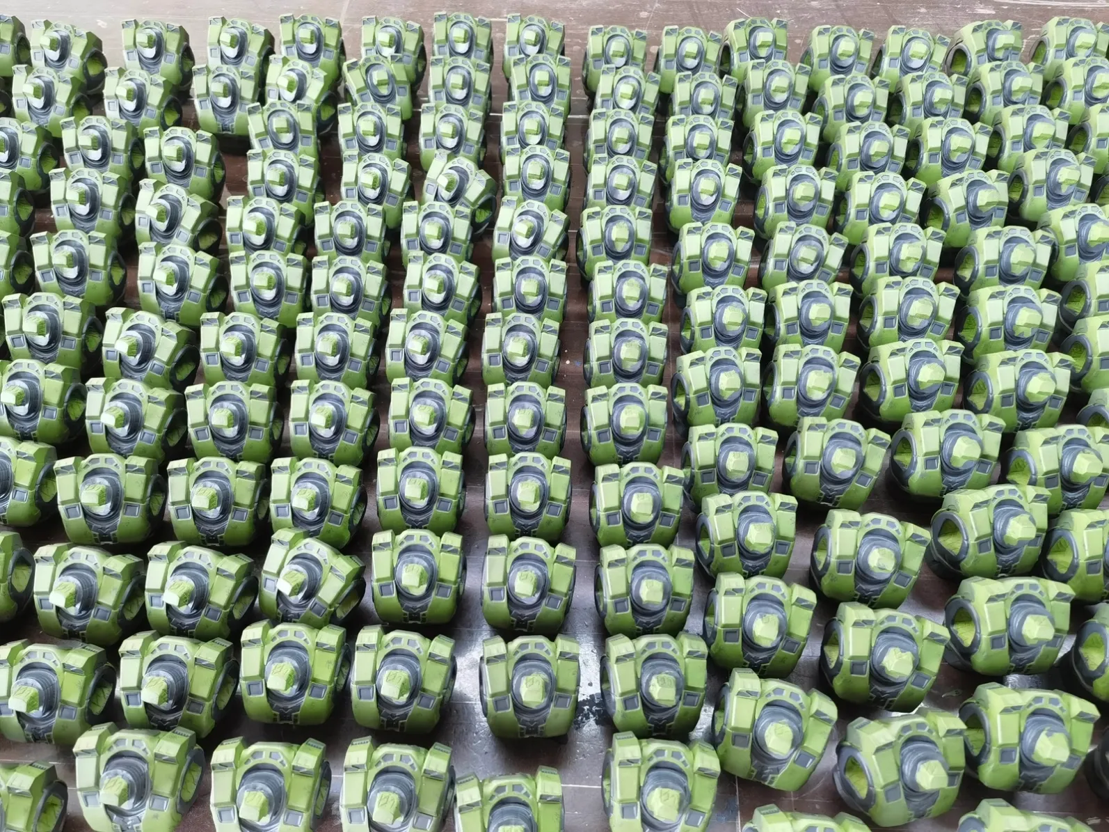 Rows of partially painted green and gray armor components with masked areas on a work surface.
