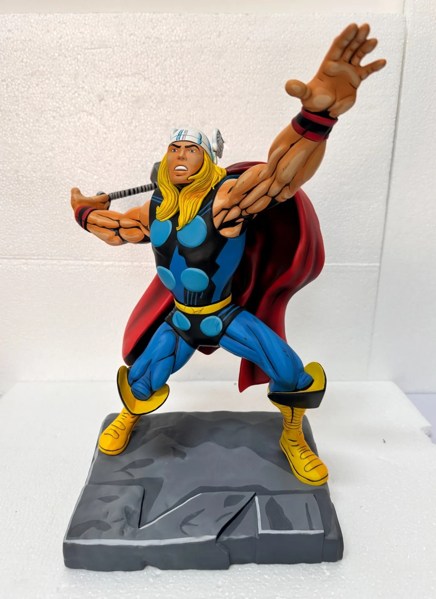 Comic-style painted collectible statue with black contour lines, hard-edged shading, a red cape and a gray scenic base.