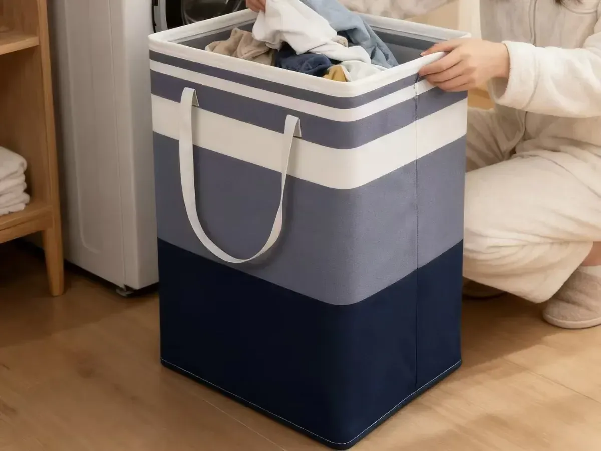 Foldable canvas laundry hamper with handles, holding clothes beside a washing machine