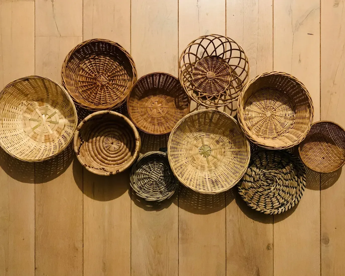A collection of handwoven natural fiber baskets in different shapes and weaves, arranged on a wooden floor