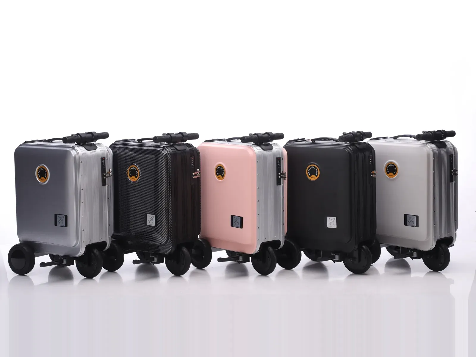 Five beautiful bird 988 ride-on electric suitcases of the same chassis and size lined up against a white studio background in five finishes: silver, carbon-fibre black, pink, matte black and light grey