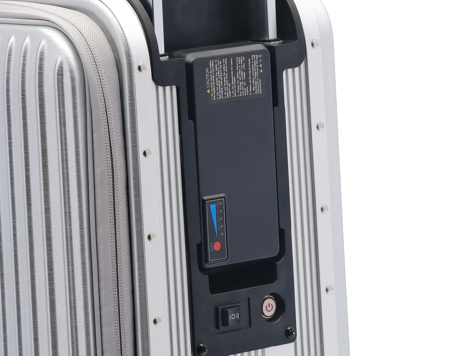 Close-up of the battery control panel on a beautiful bird 918 ride-on electric suitcase, showing the English-language lithium battery caution label with CE and WEEE marks, the battery level gauge with its red test button, and the I O II power switch
