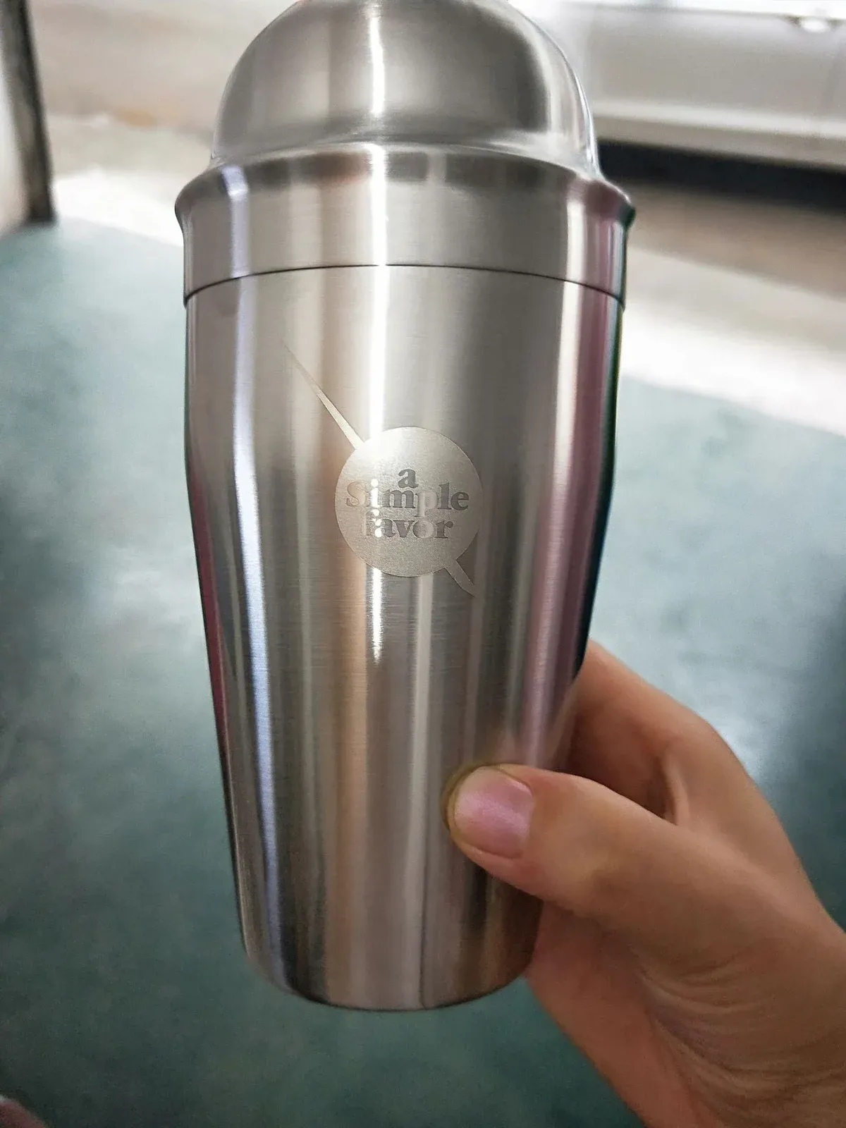 Brushed stainless steel cocktail shaker held in a hand, showing a laser-engraved logo example