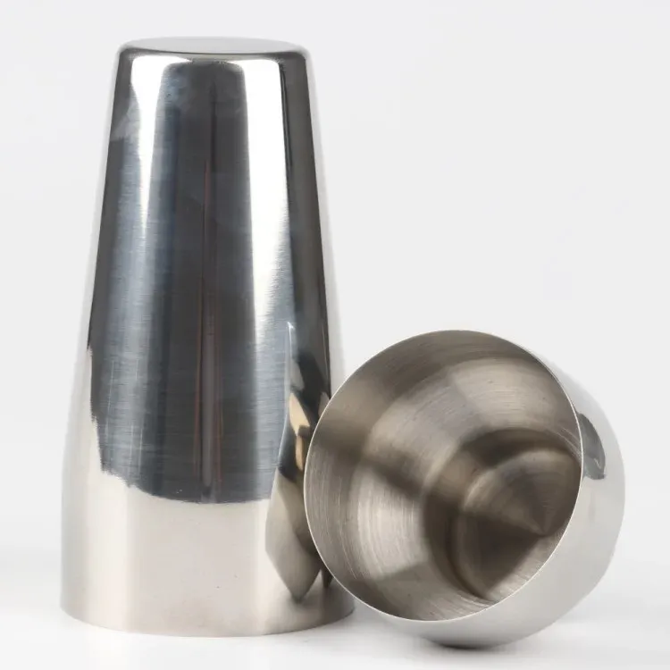 Two stainless steel cocktail shaker tins, one tipped over to show the interior, on a white background