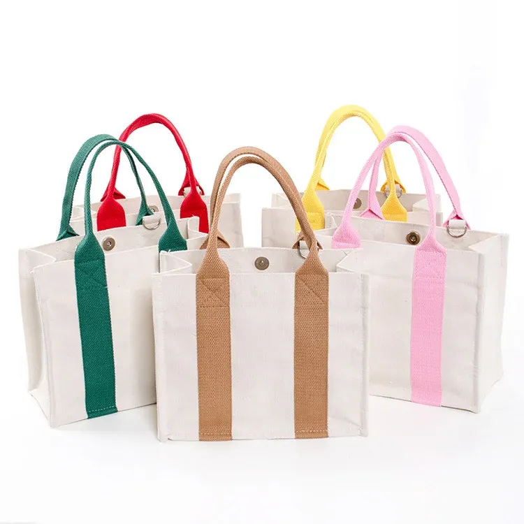 Five cream mini canvas totes with green, red, tan, yellow and pink webbing handles grouped together