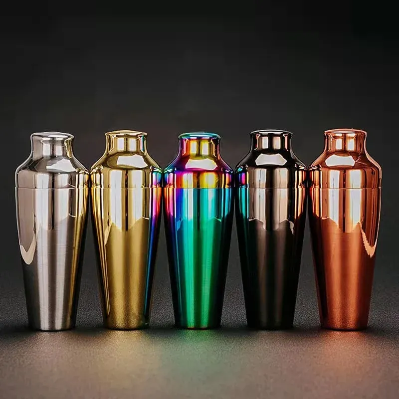 Five stainless steel cocktail shakers in silver, gold, rainbow, black and copper finishes lined up on a dark grey background