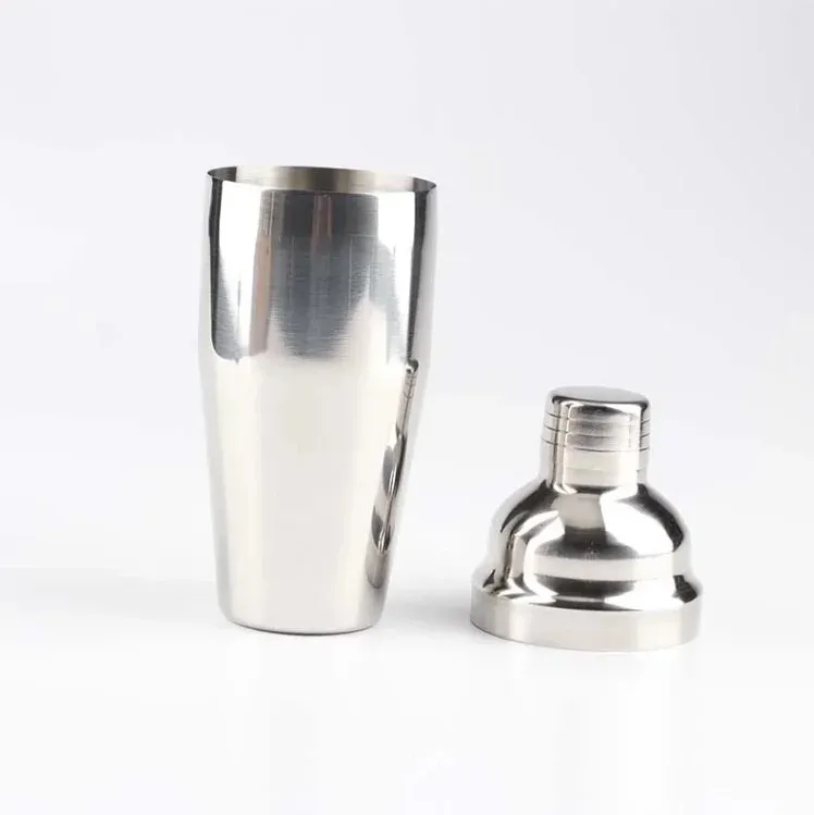 Open stainless steel cocktail shaker with its ridged cap beside the body on a white background