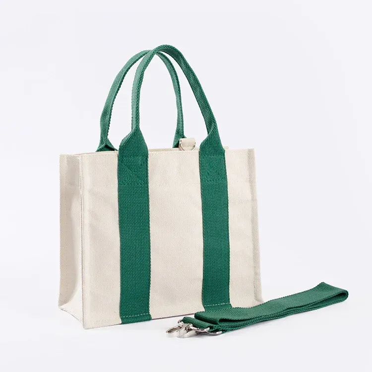 Cream mini canvas tote with green webbing handles and a detachable green shoulder strap with metal clips lying beside it