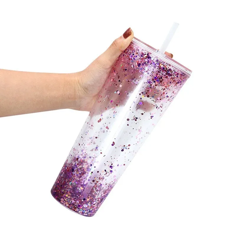 Hand holding a 24oz plastic straw tumbler with pink-purple glitter fill