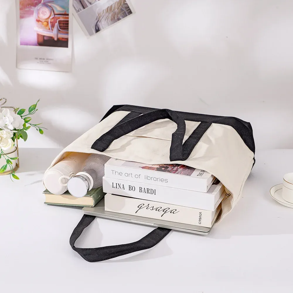 Large cream tote with black handles and base lying open and filled with books, a laptop and a bottle
