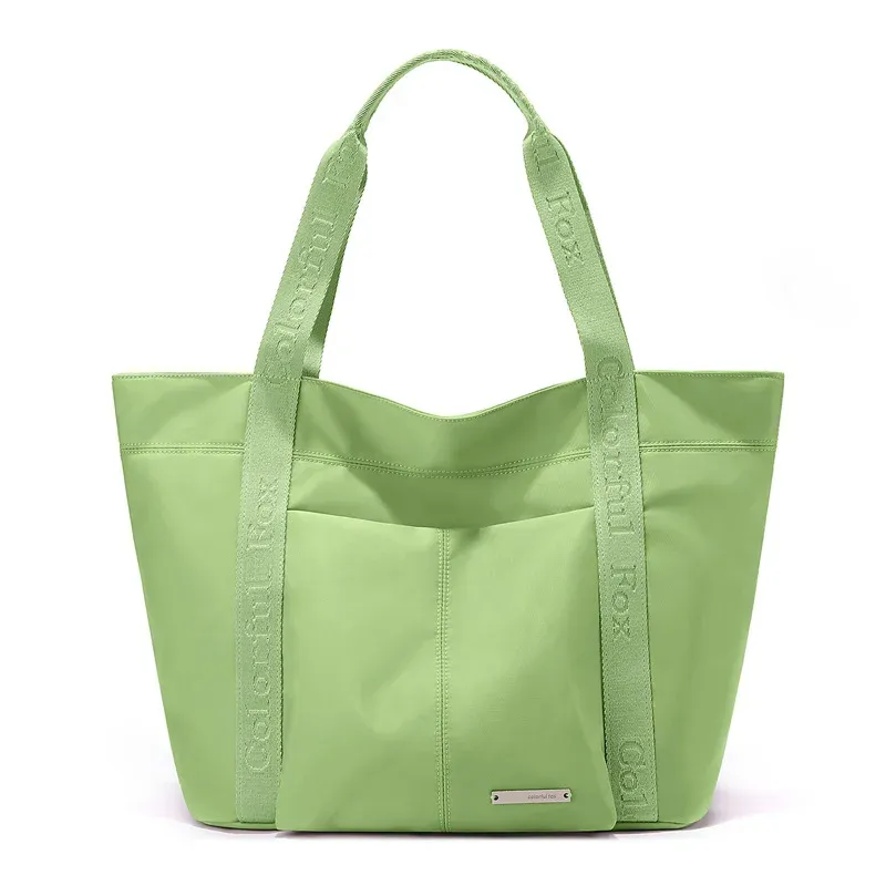 Light green nylon tote bag with front slip pocket and short webbing handles with printed text, front view