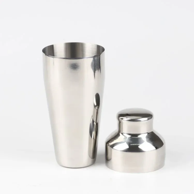 Open stainless steel cocktail shaker with its domed cap resting beside the body on a white background