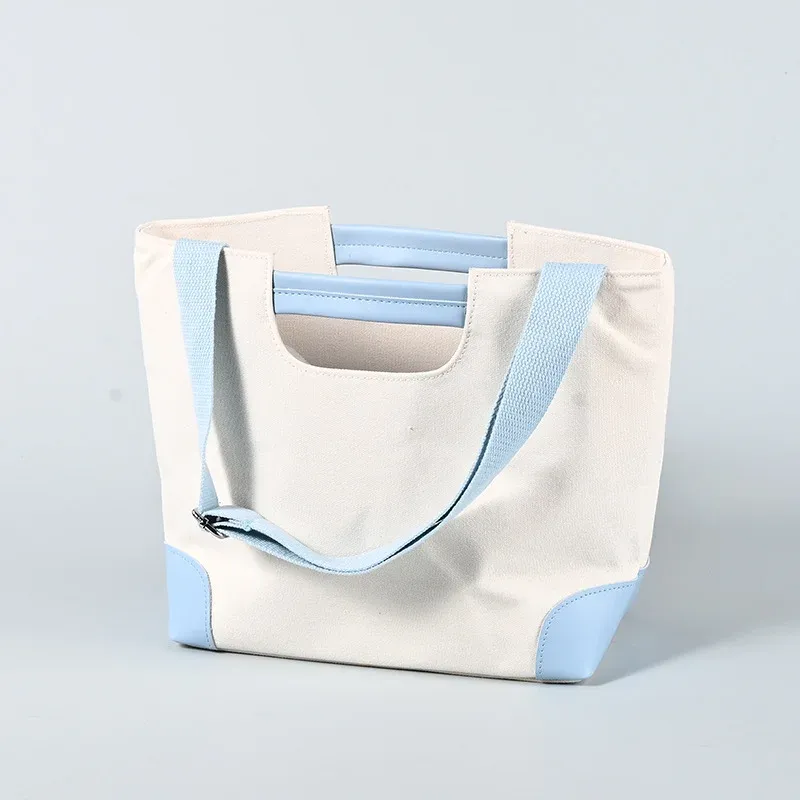 Cream canvas tote with light blue trim, padded short handle and long light blue shoulder strap