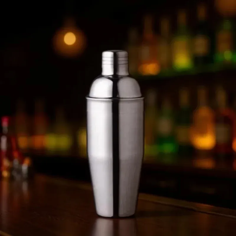 Silver stainless steel cocktail shaker standing on a bar counter with bottles blurred in the background