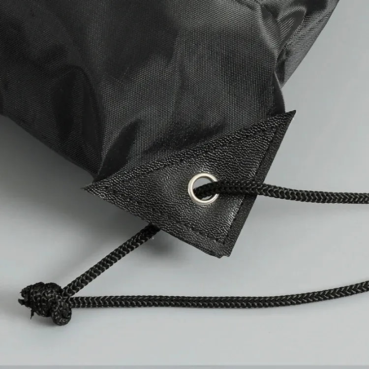 Close-up of the reinforced corner patch and metal eyelet with braided drawcord on a black drawstring backpack