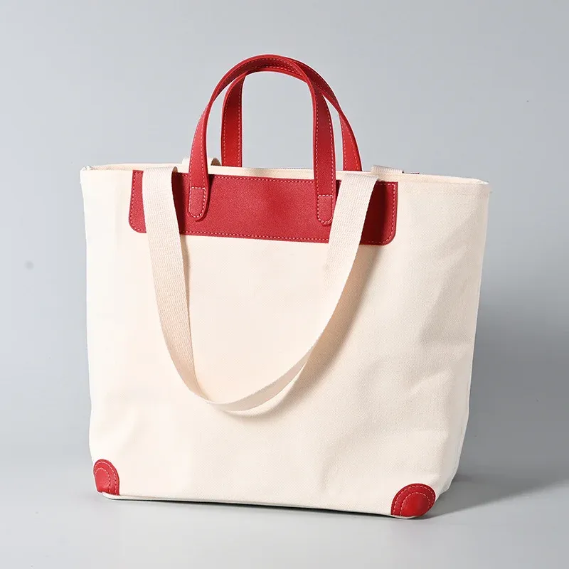 Ivory 16oz canvas tote bag with red leather short handles, trim panel and corner guards, long webbing shoulder handle draped in front