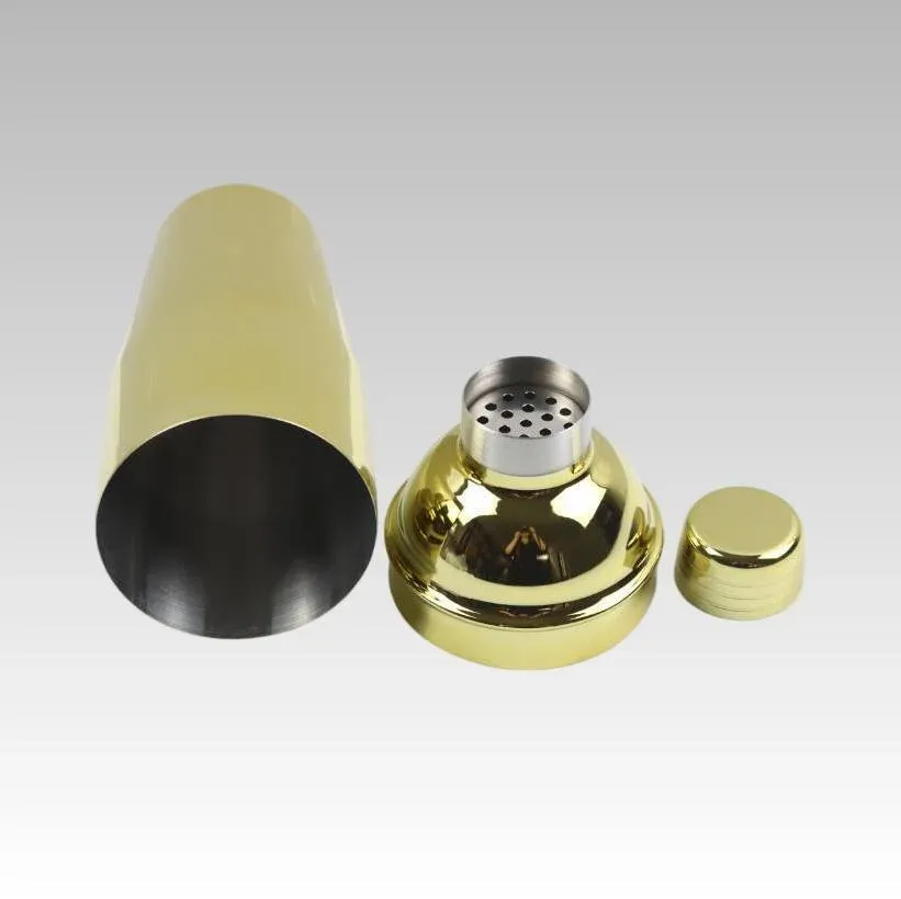 Gold cocktail shaker disassembled into body, strainer top and small cap, stainless steel interior visible