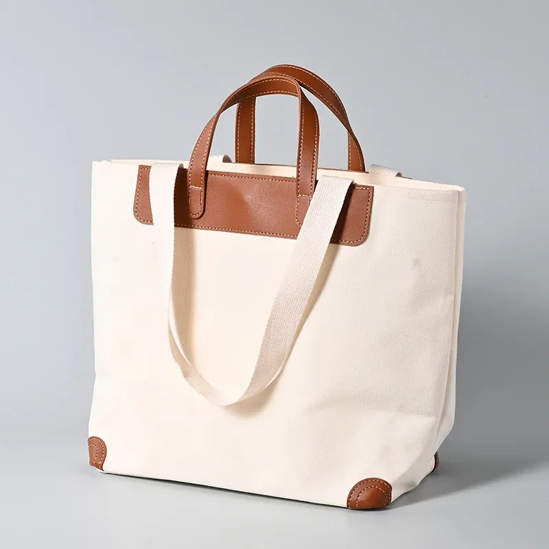 Ivory 16oz canvas tote bag with brown leather short handles, trim panel and corner guards, long webbing shoulder handle draped in front