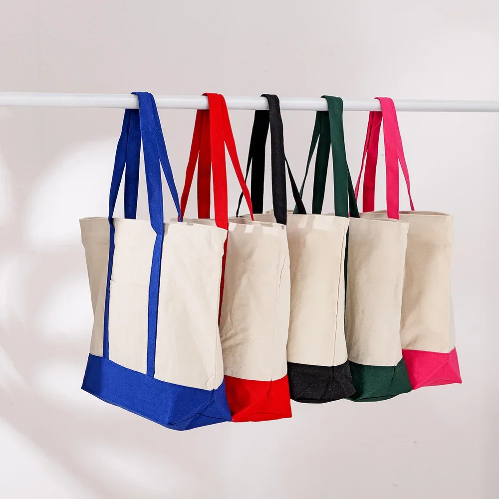 Five cream canvas totes with blue, red, black, green and pink contrast bases hanging from a rail