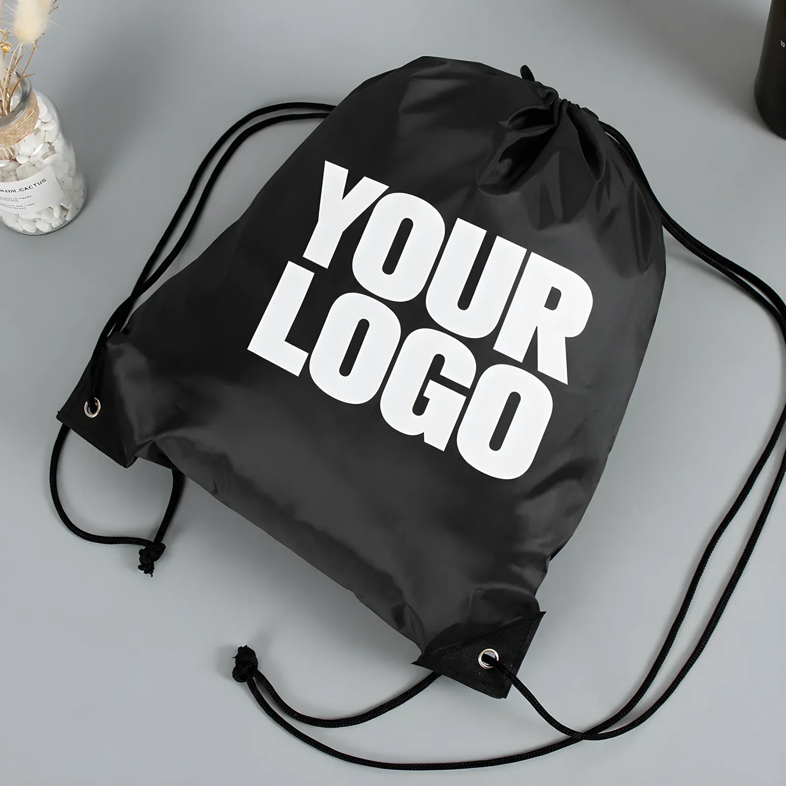 Black 210D drawstring backpack with YOUR LOGO print lying flat, angled top view