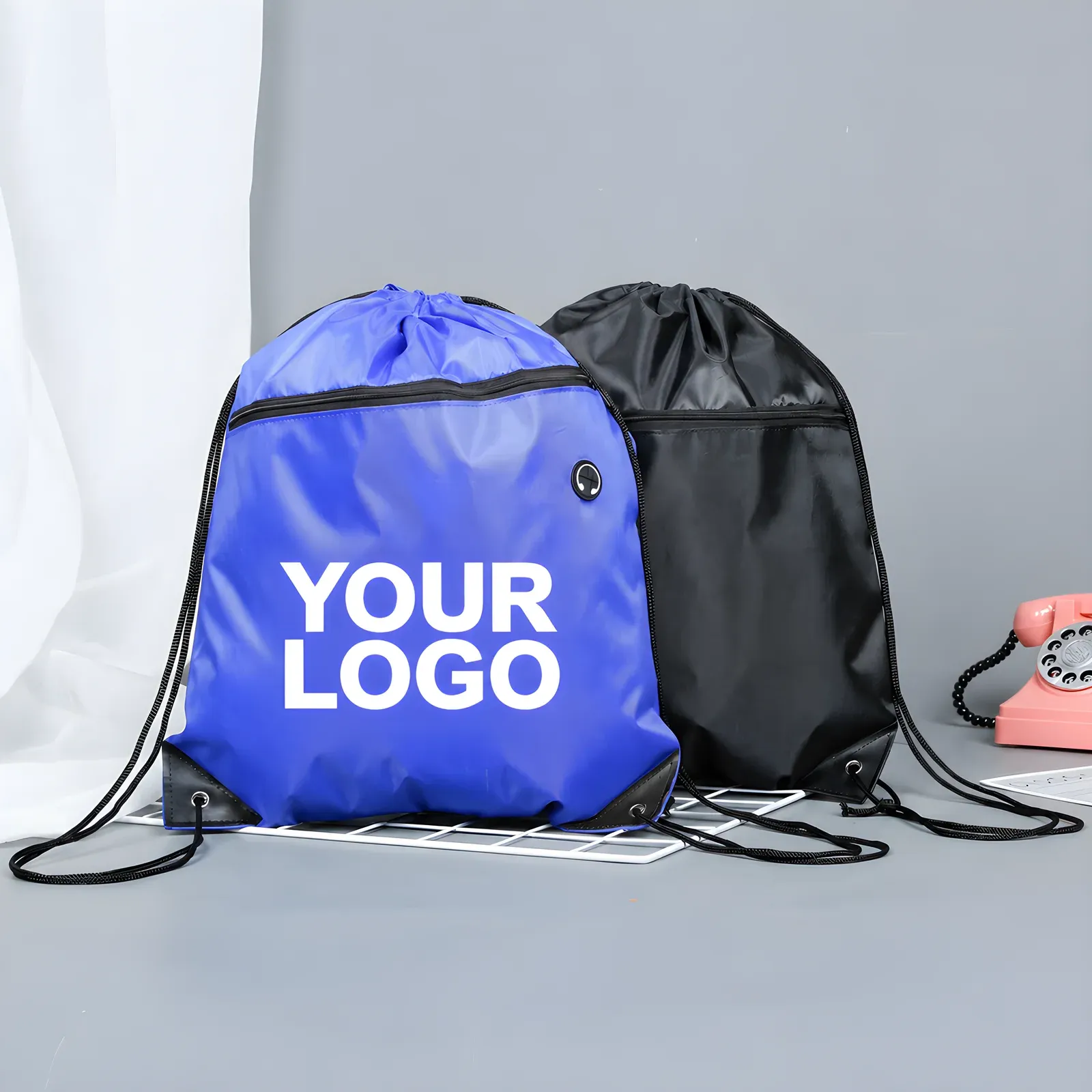 Blue and black heavy-duty 3000D drawstring backpacks with front zip pockets, blue one printed YOUR LOGO, styled on a grey studio background