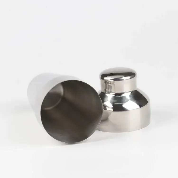 Stainless steel cocktail shaker tin and domed cap lying open on a white background