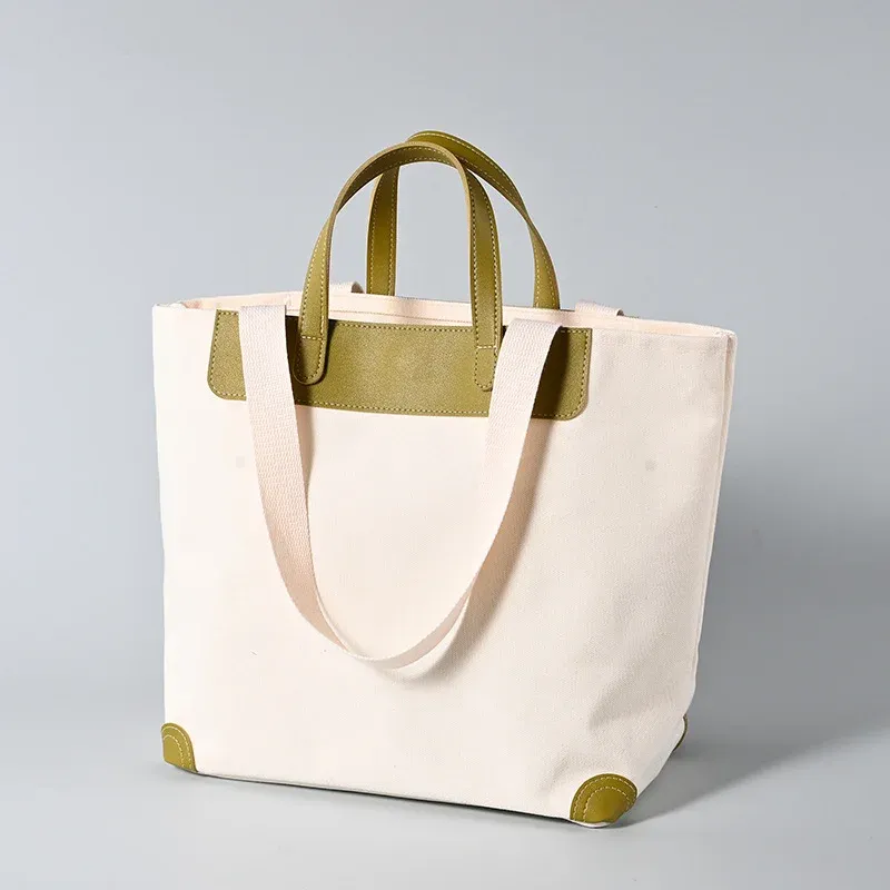 Ivory 16oz canvas tote bag with olive green leather short handles, trim panel and corner guards, long webbing shoulder handle draped in front