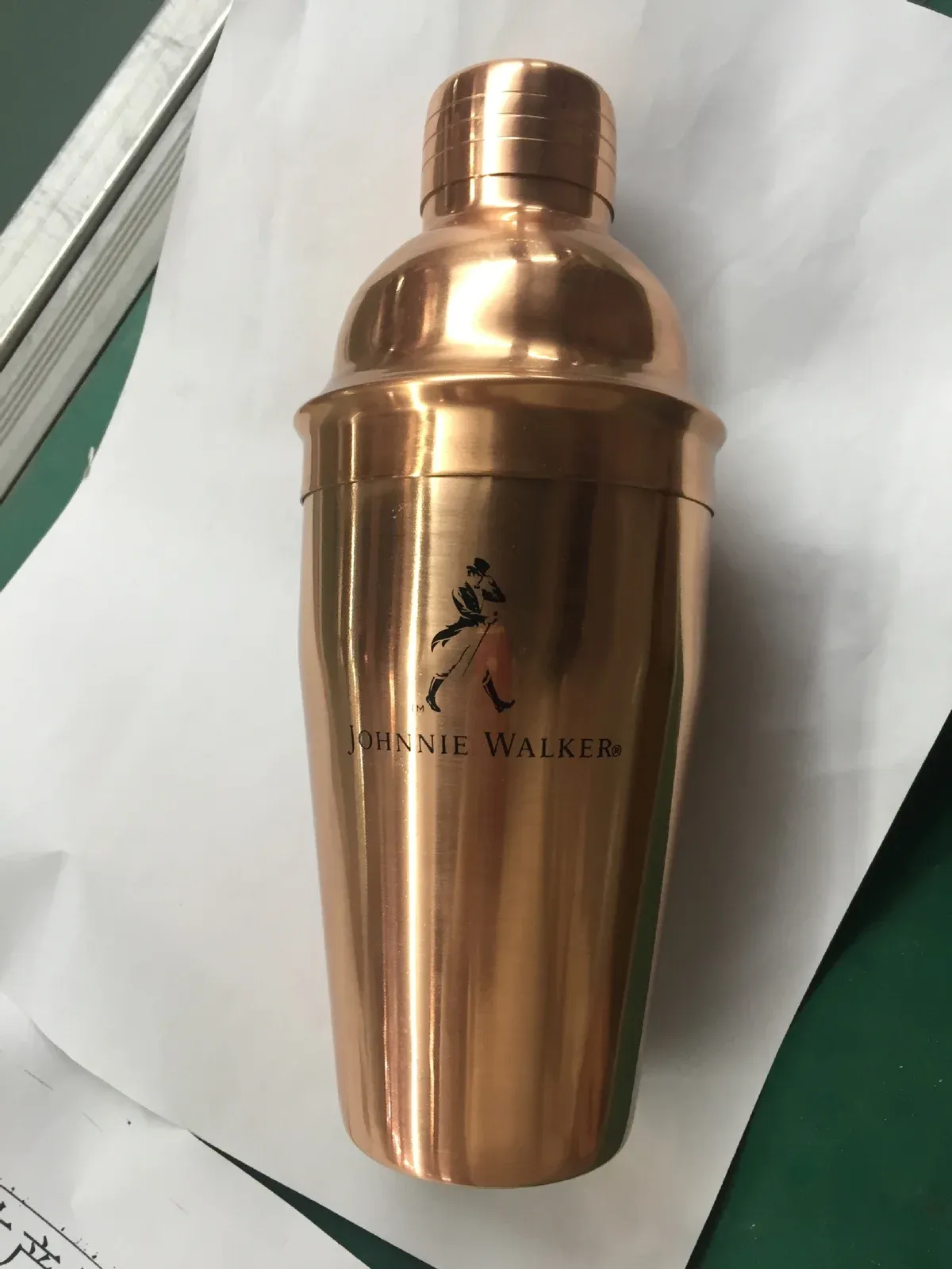 Copper-finish cocktail shaker sample with a black printed logo, photographed on a workshop table