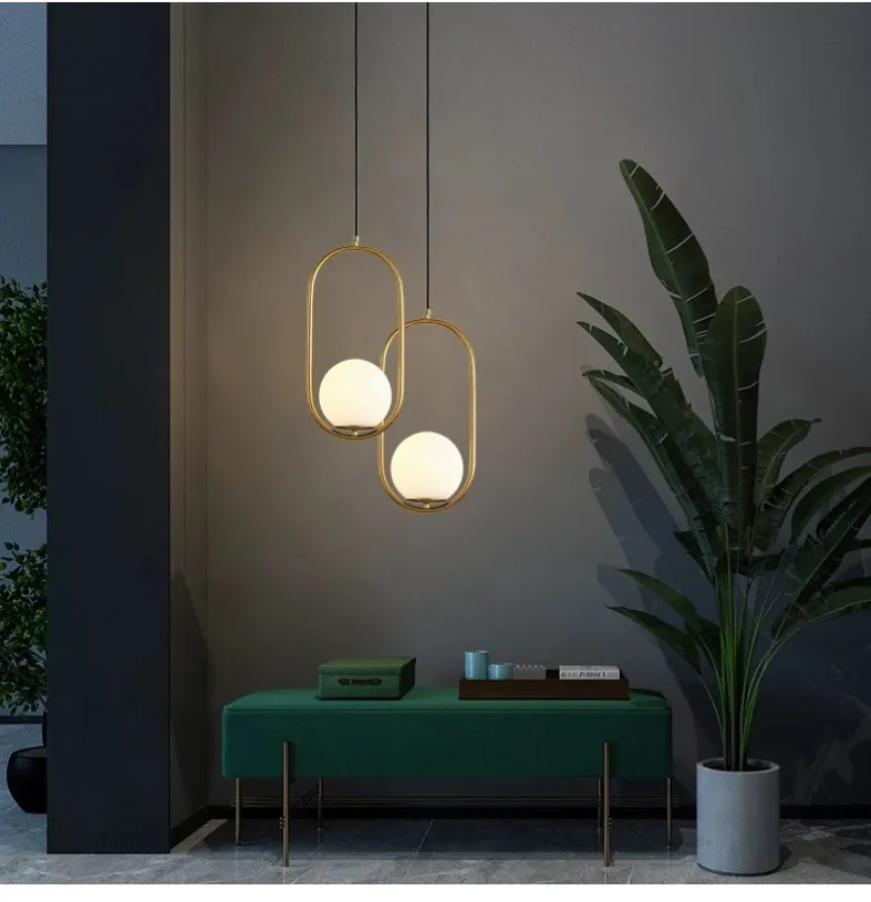 Two brass oval frame glass globe pendant lights in a modern interior above a green console table.