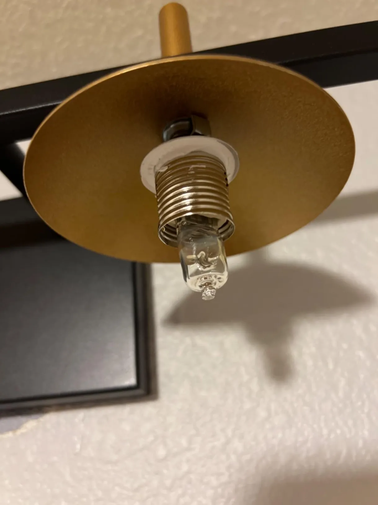 Close-up of SPW-2607 vanity wall light showing the exposed bulb holder, small capsule bulb and satin gold metal mounting plate.