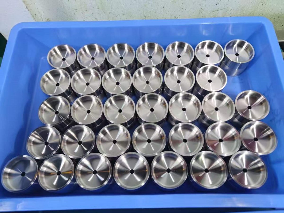 Lot of polished CNC turned steel cup parts arranged in a blue tray