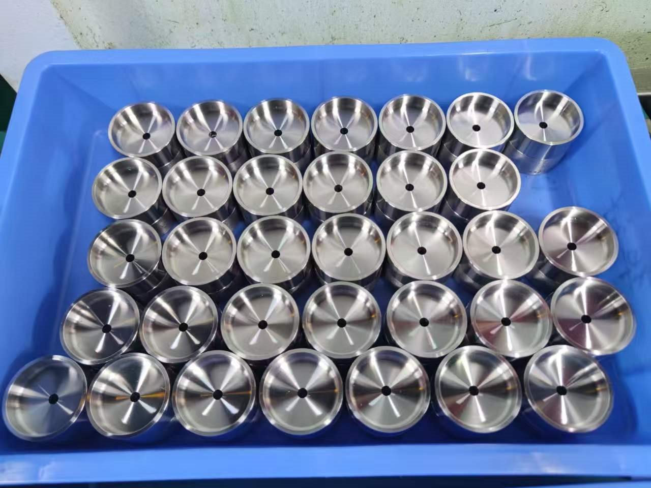 Lot of polished CNC turned steel cup parts arranged in a blue tray