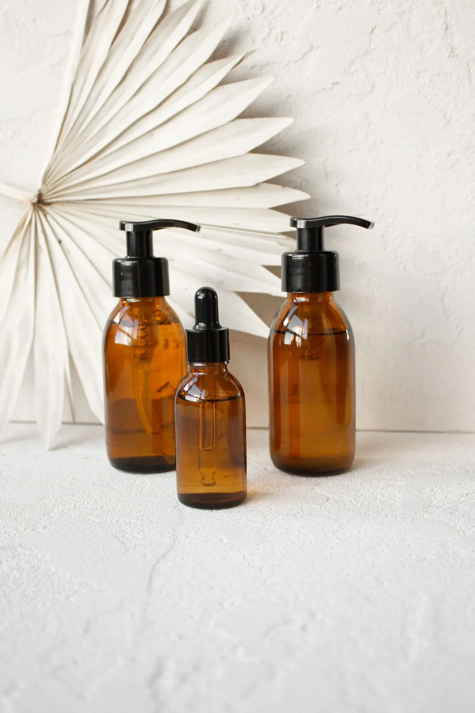 Row of amber glass pump bottles on a minimal backdrop, referencing the hair oil packaging trend toward amber glass