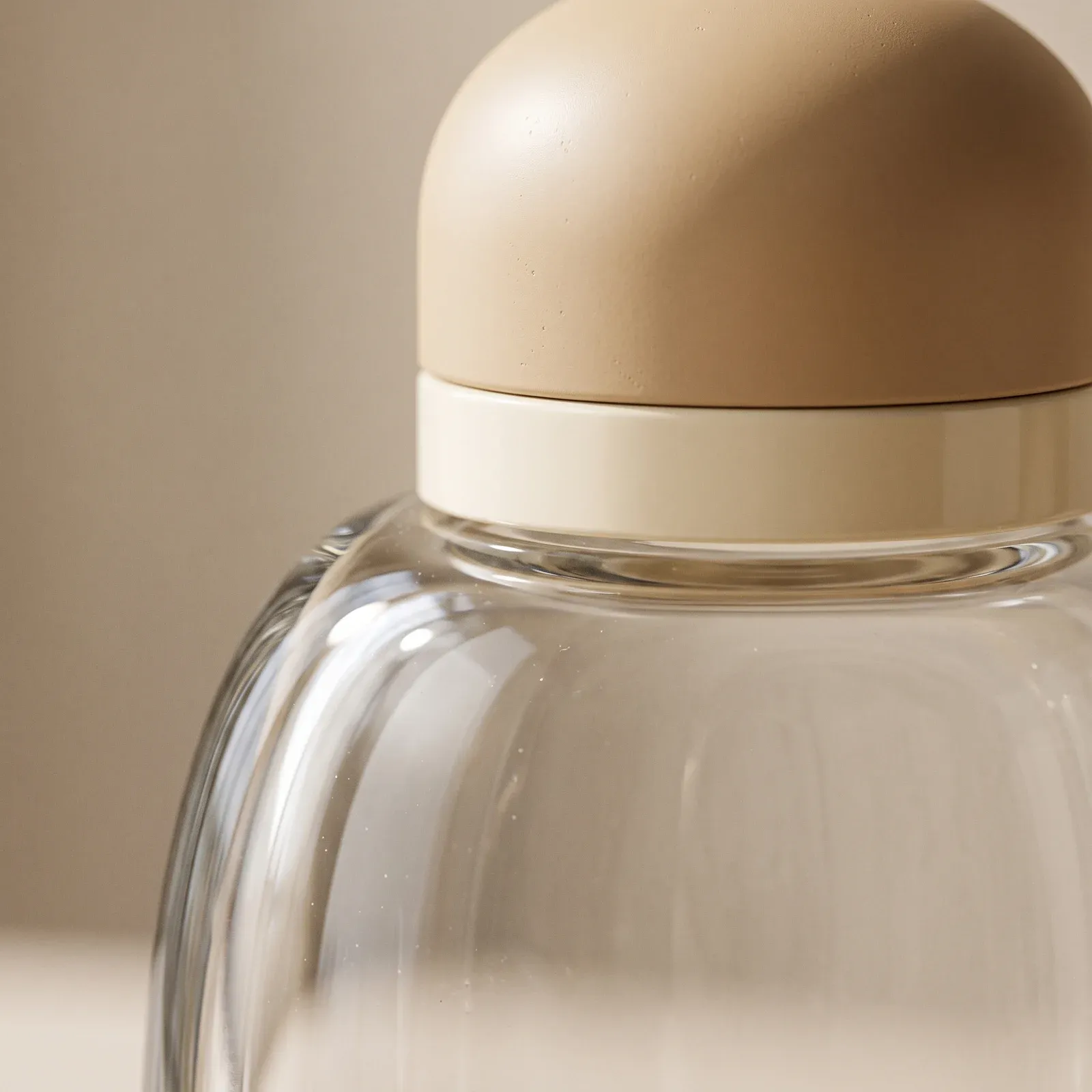 Macro detail of a sand-tone dome cap and cream collar on a thick-wall glass bottle