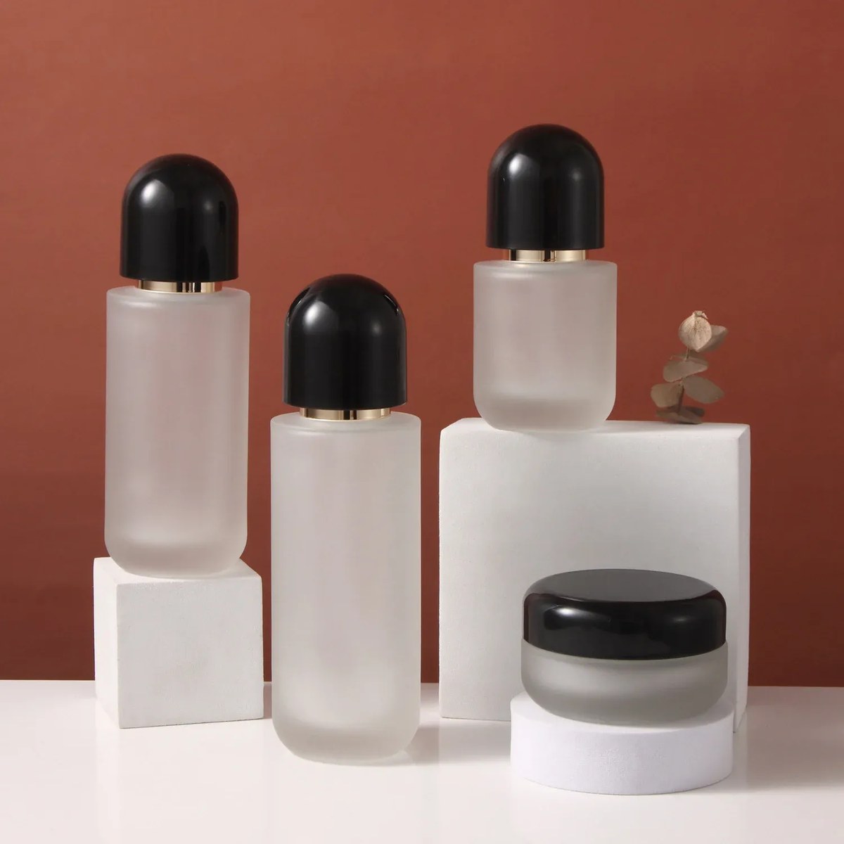 Frosted glass skincare set with black dome caps: three pump bottles and a cream jar on white blocks