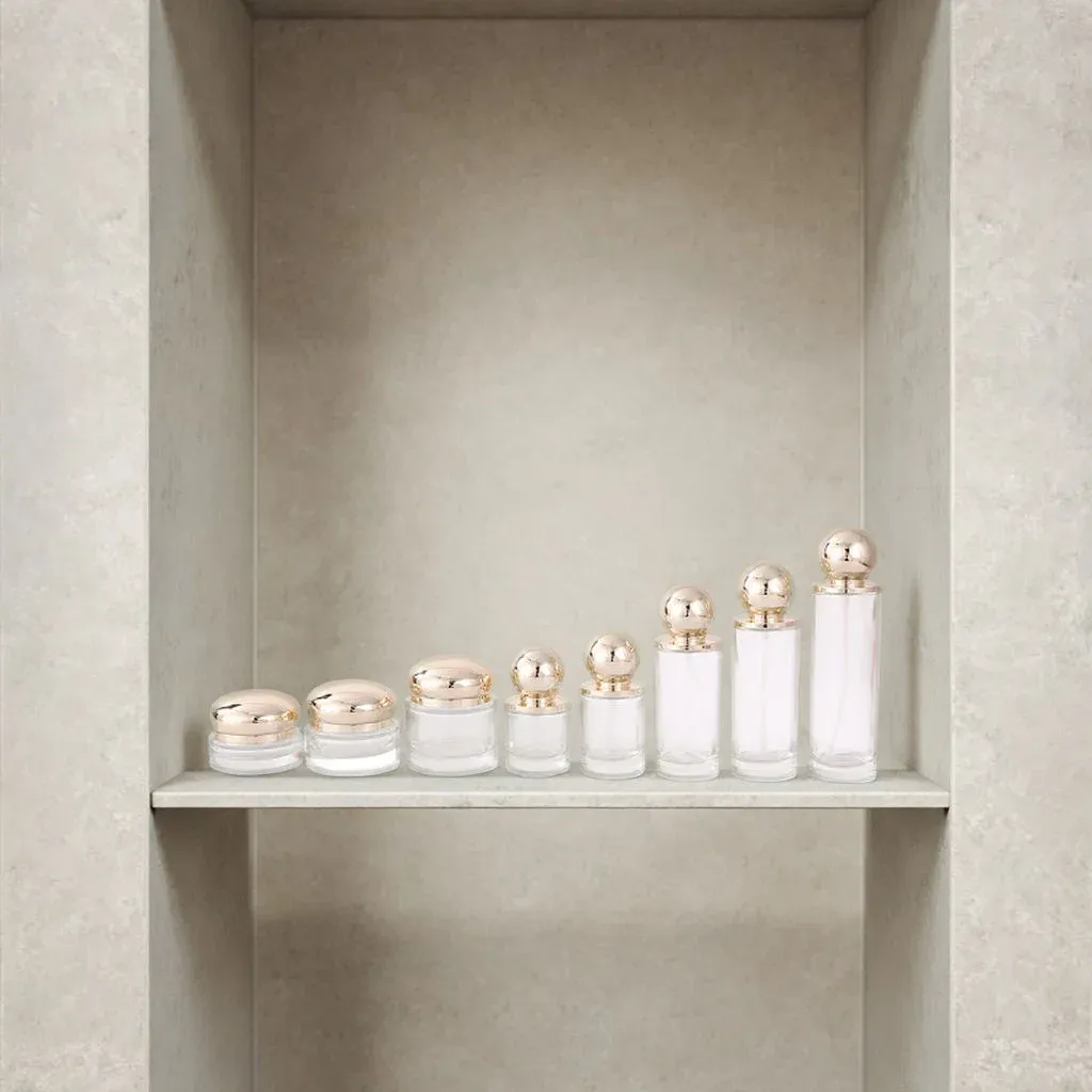 Clear glass jars and bottles with gold ball lids lined up on a concrete shelf