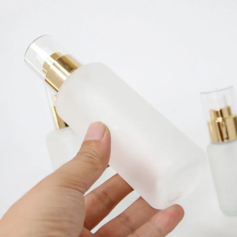 Hand holding a frosted glass spray bottle with gold collar