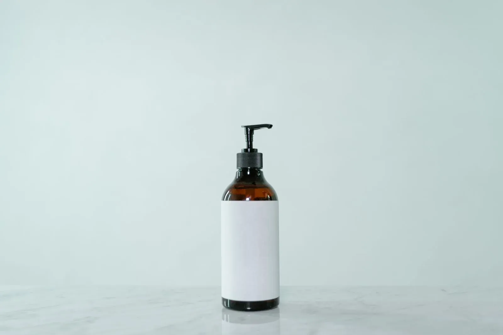 Amber glass lotion pump bottle with a blank label on a light surface