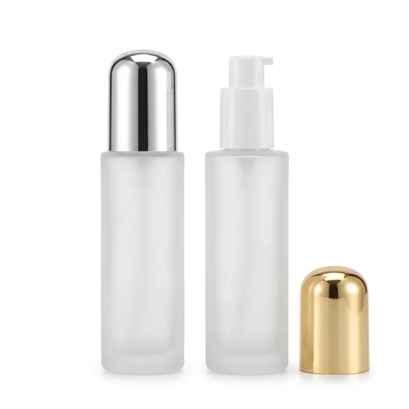 Two frosted glass cylindrical pump bottles on white background: one with a polished silver dome overcap, one with the white lotion pump exposed and its gold dome overcap resting beside