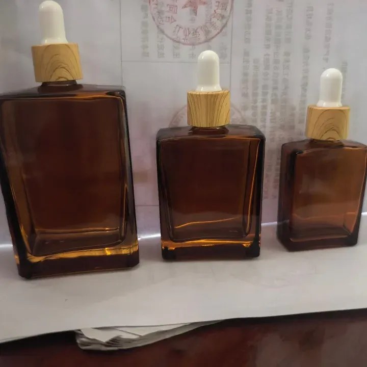 Three square-shouldered amber glass dropper bottles in 15 ml, 30 ml and 50 ml with white-bulb droppers and wood-look collars