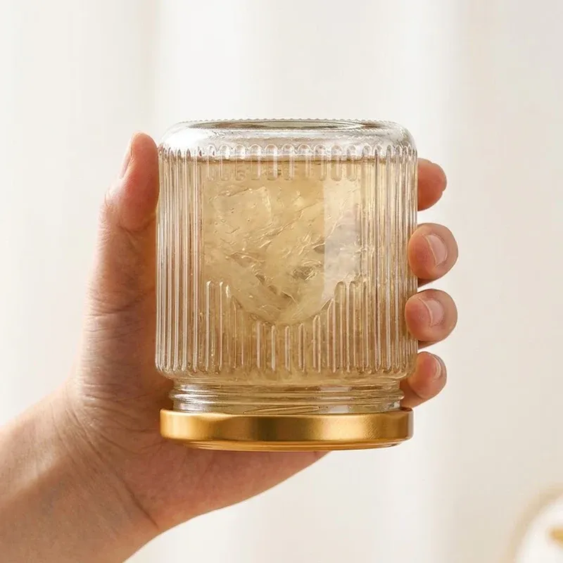 A hand holding the squat ribbed glass jar upside down with its gold lid facing down, demonstrating the factory's inverted no-drip seal demo