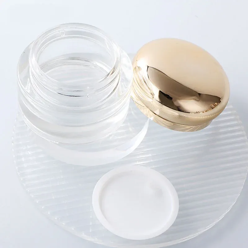 Open clear glass cream jar with gold ball lid and white inner liner
